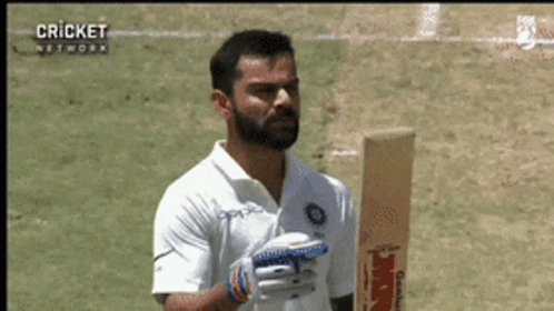 A Man With A Beard Is Holding A Cricket Bat On A Field GIF