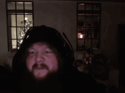 A Man With A Beard Is Holding A Donut In Front Of A Christmas Tree In A Dark Room . GIF