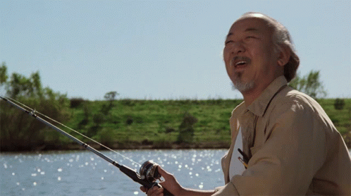 A Man With A Beard Is Holding A Fishing Rod In Front Of A Body Of Water GIF