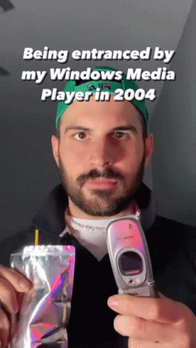 A Man With A Beard Is Holding A Flip Phone And A Bag Of Food GIF