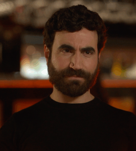 A Man With A Beard Is Holding A Glass In Front Of His Face GIF