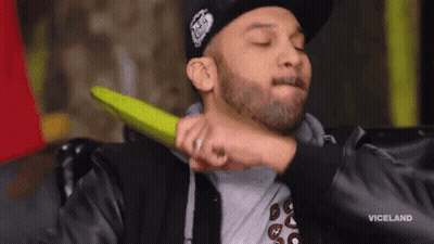 A Man With A Beard Is Holding A Green Object To His Neck . GIF