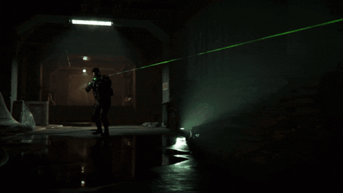 A Man With A Beard Is Holding A Gun In A Dark Room With Green Lights Coming Out Of His Face . GIF