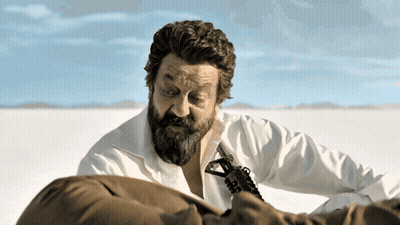 A Man With A Beard Is Holding A Gun In A Field GIF