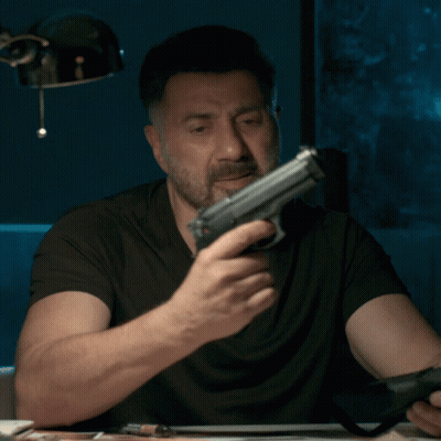 A Man With A Beard Is Holding A Gun In His Right Hand GIF