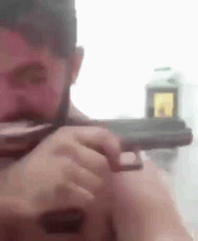 A Man With A Beard Is Holding A Gun In His Right Hand . GIF