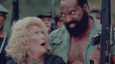 A Man With A Beard Is Holding A Gun Next To A Woman GIF