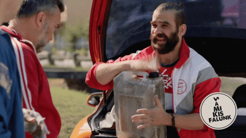 A Man With A Beard Is Holding A Jerry Can In Front Of A Sign That Says Mi Kis Falunk GIF