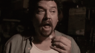 A Man With A Beard Is Holding A Key To His Chest In A Dark Room . GIF