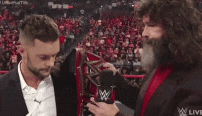 A Man With A Beard Is Holding A Microphone And Talking To Another Man In A Suit . GIF