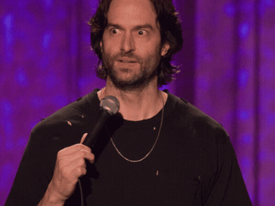a man with a beard is holding a microphone in front of a purple curtain