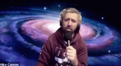 A Man With A Beard Is Holding A Microphone In Front Of A Spiral Galaxy . GIF