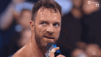 A Man With A Beard Is Holding A Microphone In Front Of His Face . GIF