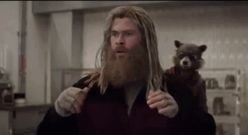 A Man With A Beard Is Holding A Raccoon On His Shoulder In A Kitchen . GIF