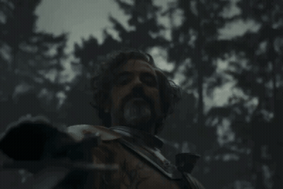 A Man With A Beard Is Holding A Sword In A Dark Forest GIF
