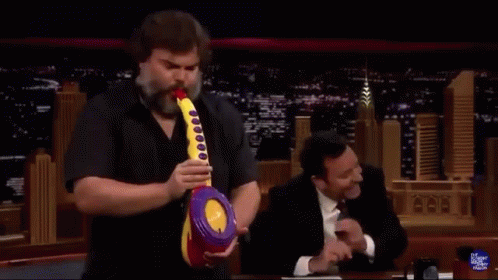 A Man With A Beard Is Holding A Toy Saxophone In Front Of Jimmy Fallon GIF