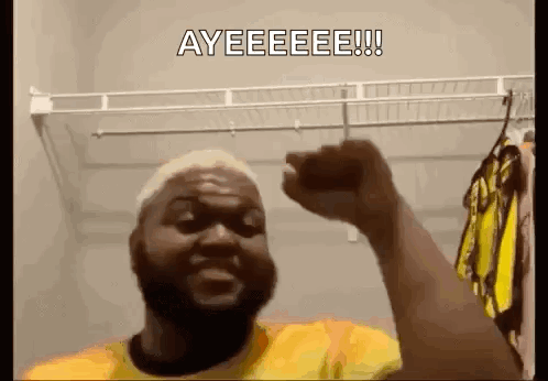 A Man With A Beard Is Holding His Fist Up In The Air In A Closet . GIF