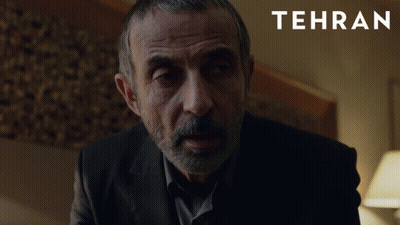 A Man With A Beard Is In A Dark Room With Tehran Written On The Bottom GIF