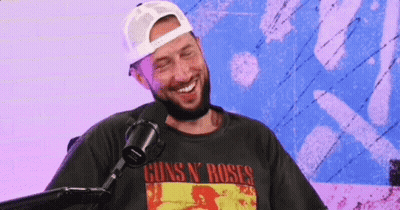 A Man With A Beard Is Laughing In Front Of A Microphone Wearing A Guns N ' Roses Shirt . GIF