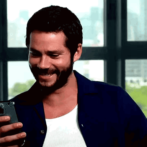 A Man With A Beard Is Laughing While Looking At His Phone GIF