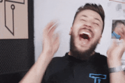 A Man With A Beard Is Laughing With His Mouth Open And His Hands In The Air . GIF