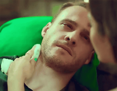 A Man With A Beard Is Laying Down With A Woman Holding His Neck GIF