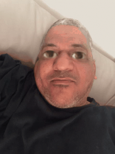 A Man With A Beard Is Laying In A Bed And Looking At The Camera GIF