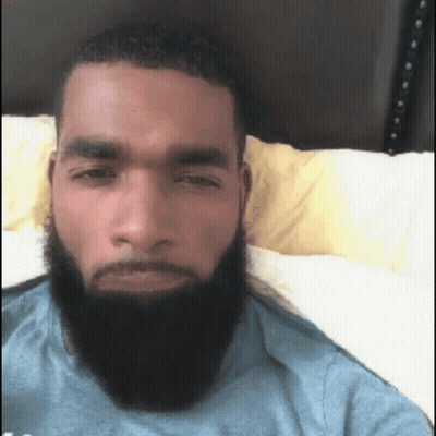 A Man With A Beard Is Laying In Bed And Looking At The Camera . GIF