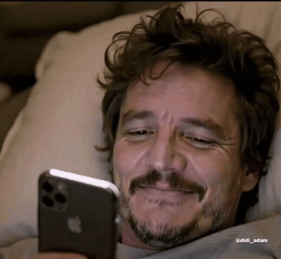 A Man With A Beard Is Laying In Bed Looking At His Iphone . GIF