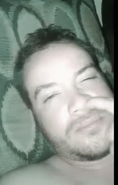 A Man With A Beard Is Laying In Bed With His Eyes Closed . GIF