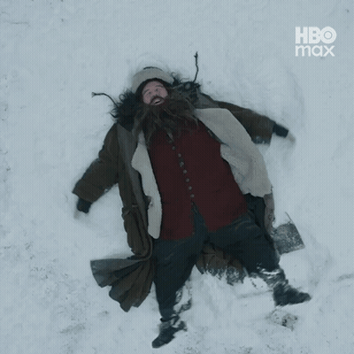 A Man With A Beard Is Laying In The Snow With Hbo Max In The Corner GIF