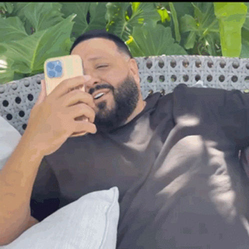 A Man With A Beard Is Laying On A Couch And Looking At His Phone GIF