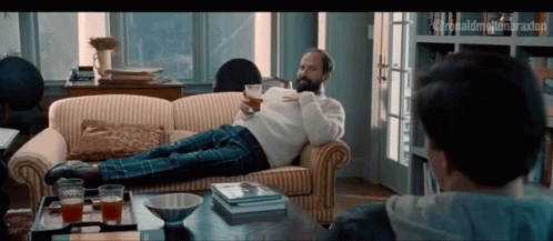 A Man With A Beard Is Laying On A Couch With A Cup Of Coffee In His Hand GIF