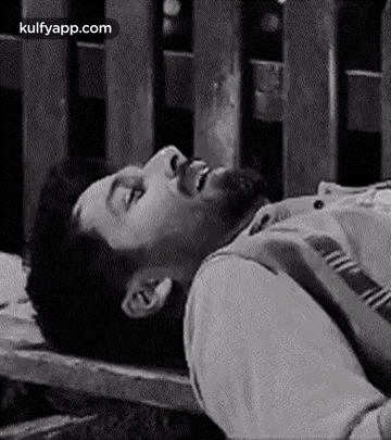 A Man With A Beard Is Laying On A Wooden Bench With His Eyes Closed . GIF