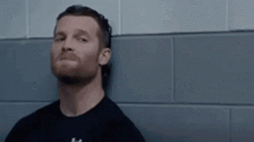 A Man With A Beard Is Leaning Against A Wall With The Word Hell On It . GIF