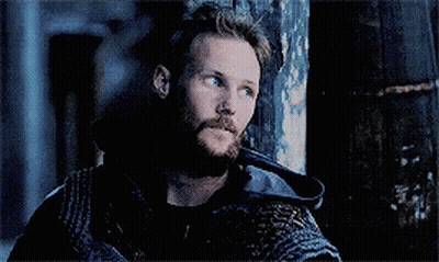 a man with a beard is leaning against a wooden wall in a dark room .