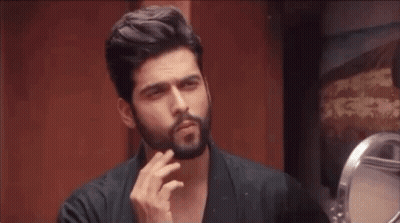 A Man With A Beard Is Looking At Himself In The Mirror GIF