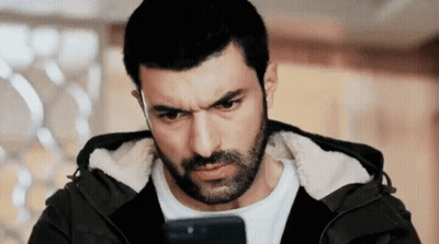 A Man With A Beard Is Looking At His Cell Phone And Making A Funny Face . GIF
