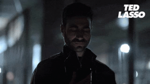 A Man With A Beard Is Looking At His Phone With Ted Lasso Written On The Bottom GIF