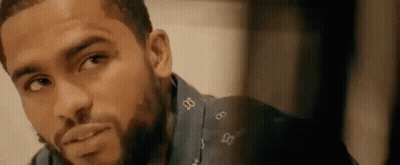A Man With A Beard Is Looking At The Camera And Smiling . GIF