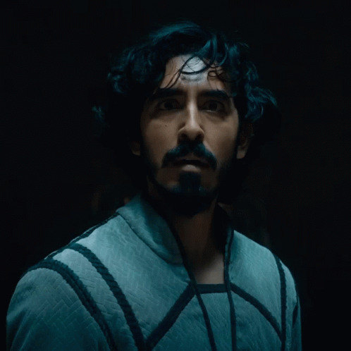 A Man With A Beard Is Looking At The Camera In A Dark Room GIF