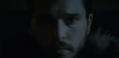 A Man With A Beard Is Looking At The Camera In The Dark . GIF
