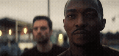A Man With A Beard Is Looking At The Camera While Another Man Looks On . GIF