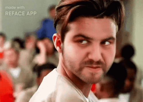 A Man With A Beard Is Looking At The Camera With A Crowd Of People In The Background . GIF
