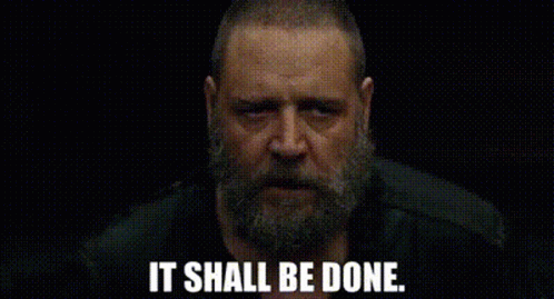 A Man With A Beard Is Looking At The Camera With The Words `` It Shall Be Done '' Written Below Him . GIF