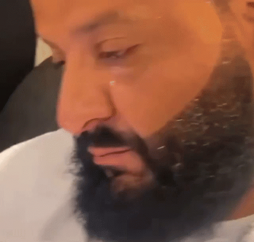 A Man With A Beard Is Looking Down At Something . GIF