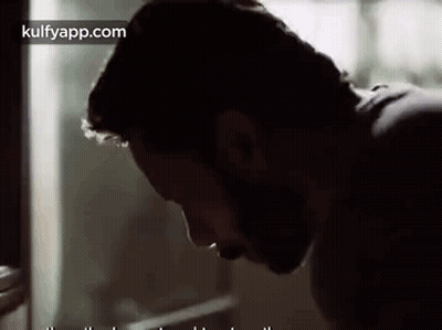 A Man With A Beard Is Looking Down At Something . GIF