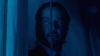 A Man With A Beard Is Looking Through A Window With A Blue Light Behind Him GIF
