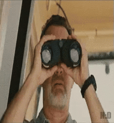 A Man With A Beard Is Looking Through Binoculars With The Letter H On The Bottom Left GIF