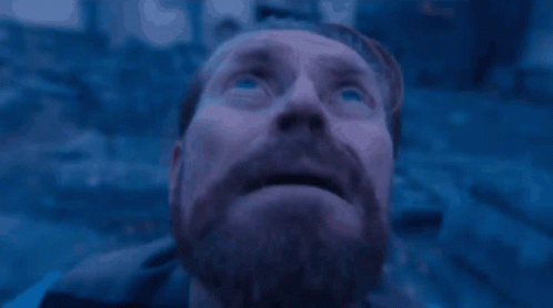 A Man With A Beard Is Looking Up At The Sky In A Blue Light . GIF